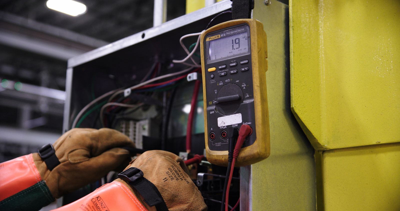 Manos con guantes realizando mediciones con multímetro en un tablero eléctrico