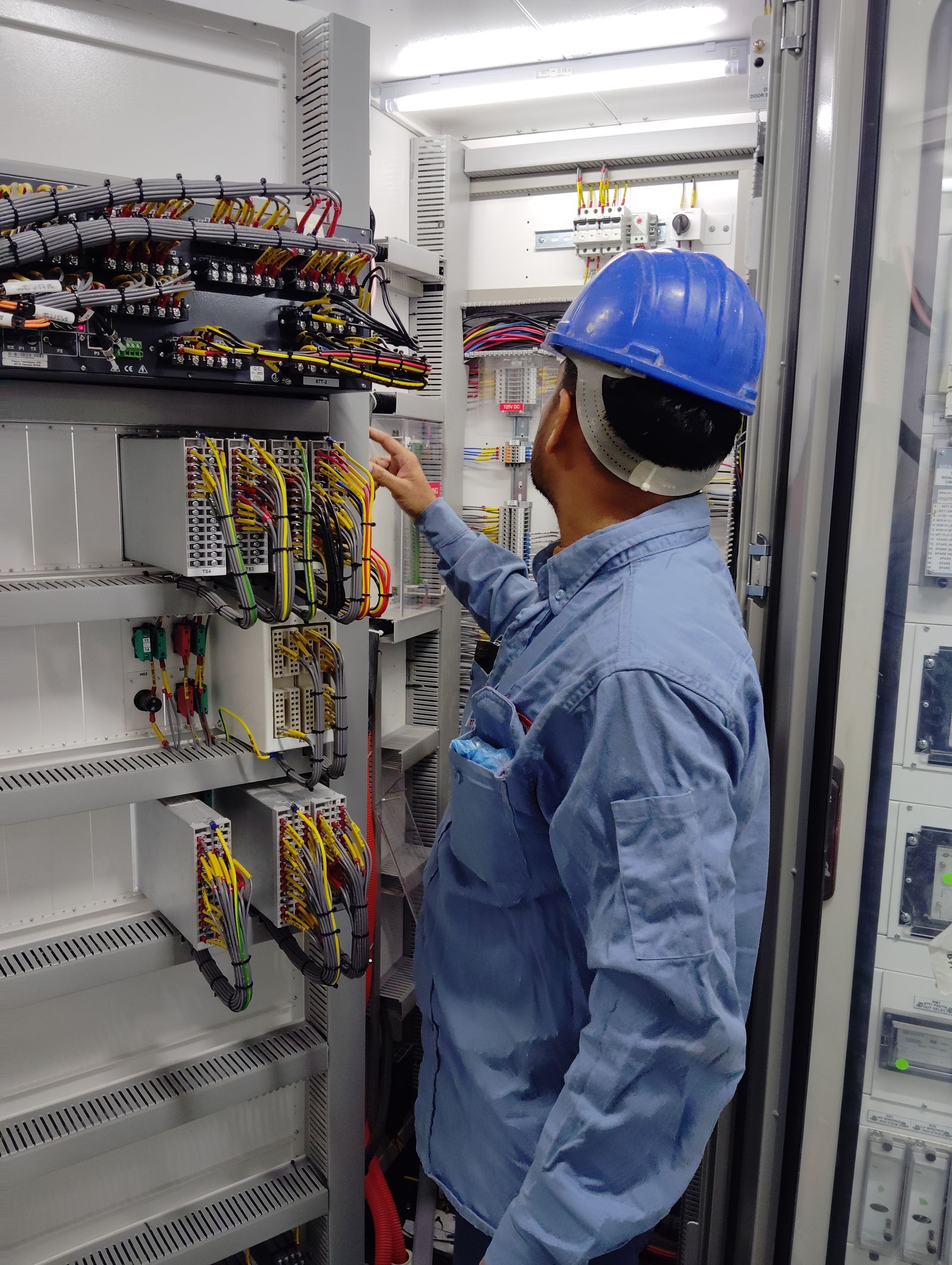 Electricista con casco inspeccionando el cableado de un tablero industrial