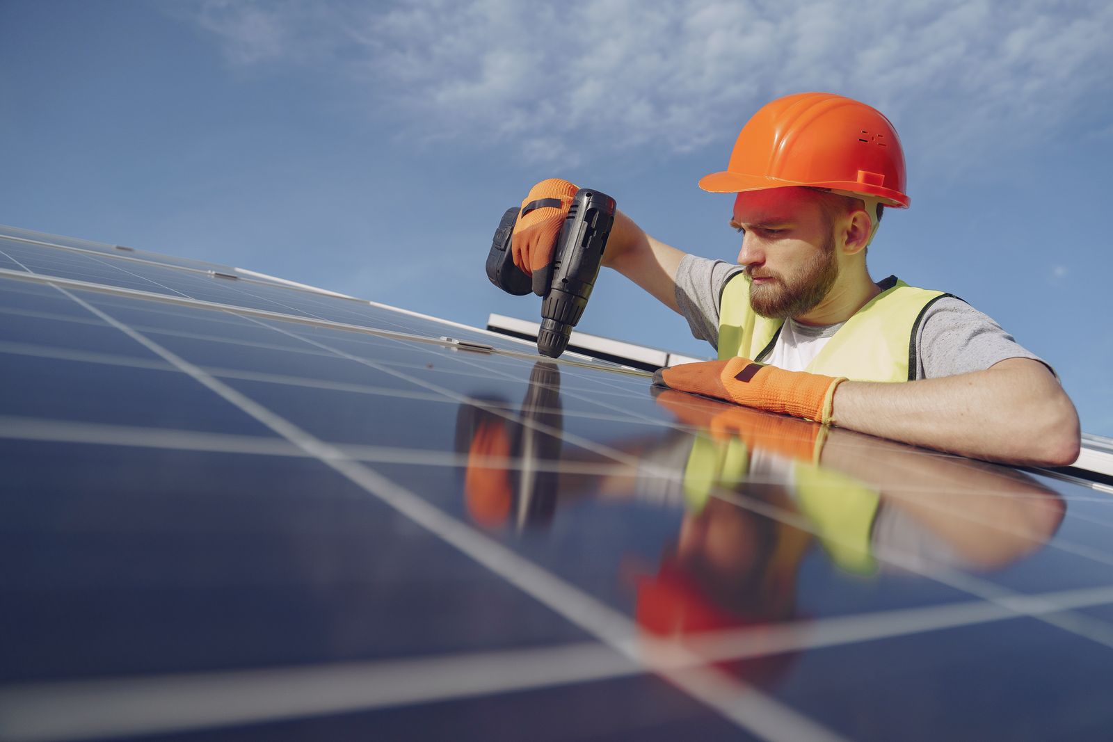 Instalador con casco y guantes fijando un panel solar con herramienta eléctrica